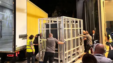 The tapestry arring in a crate being loaded from a yellow van in the middle of the night