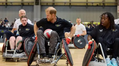 PA Media Prince Harry playing wheelchair football, sitting in a black and red wheelchair with a ball between his legs 