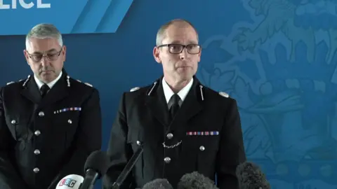 PA Media Assistant Chief Constable Matt Longman speaks to reporters at a press conference, with microphones in front of him  