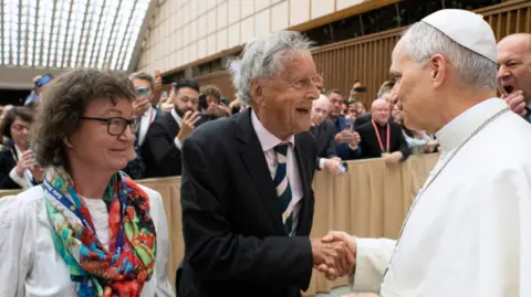 Vatican Media David Willey, seen here in the centre wearing a suit, shakes the hand of Pope Leo with his former producer Gillian Hazell last year.