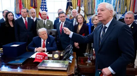 Getty Images US Senator Lindsey Graham speaks to the press alongside US President Donald Trump, surrounded by members of Congress, in the Oval Office in February 2026