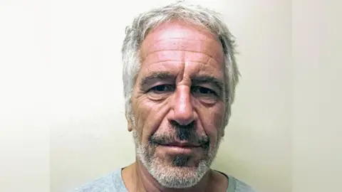 Getty Images Close-up portrait of Jeffrey Epstein taken in jail in 2019, with short grey hair and a grey beard, facing the camera against a plain light-coloured background. The image is tightly cropped around the head and shoulders, with even indoor lighting and no visible text or other objects.