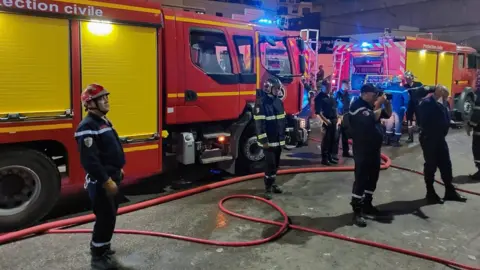 Algeria's General Directorate for Civil Protection Firefighters in blue uniforms stand in front of fire trucks
