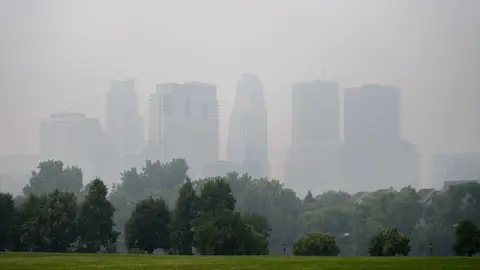 Getty Images The Minneapolis, Minnesota skyline is blurred by smoke, with green park grass and trees in the foreground