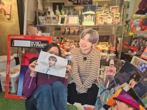 Yeon-su poses next to BTS merchandise at a BTS-themed café near HYBE headquarters in Seoul.