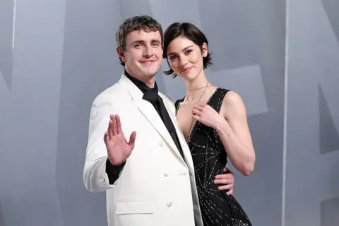 Getty Images Gracie Abrams and Paul Mescal on the red carpet of the Vanity Fair Oscars Party in 2026. Mescal is wearing a white suit, and waving at the camera. Abrams smiles as the actor puts his other arm around her waist.