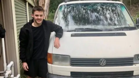 Supplied: Myfanwy Webb A teenage boy dressed in black stands next to a white van with his arm on the bonnet