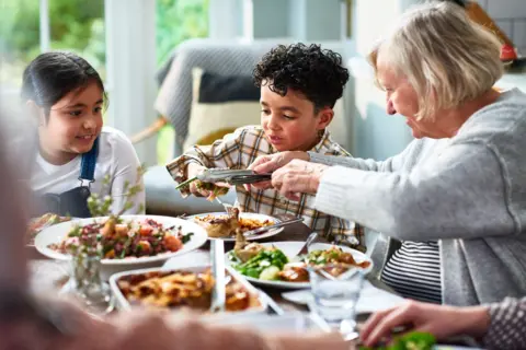 Getty Images Grandmother and children with group of relatives sitting at dining table enjoying home-cooked meal