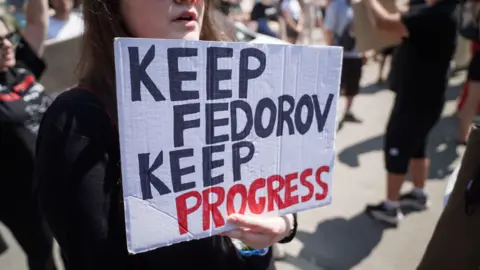 Matthew Goddard/BBC A young woman holds a sign which says 'KEEP FEDOROV, KEEP PROGRESS' 