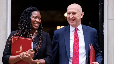 EPA Miatta Fahnbulleh and John Healey grinning as they walk out of the door at 10 Downing Street clutching red ministerial folders