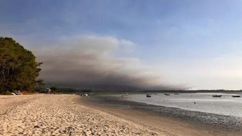 Joanna Kent/BBC Dark smoke can be seen on the skyline from the beach