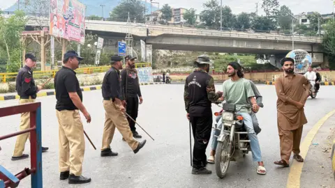 Getty Images Police frisk people at a checkpoint in Muzaffarabad, the capital of Pakistan-administered Kashmir on July 15, 2026. Nine people were killed and a dozen wounded in renewed clashes between supporters of a banned protest group and security forces in Pakistan-administered Kashmir, an official said on July 15. (Photo by Sajjad QAYYUM / AFP via Getty Images)