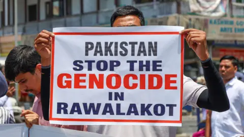 Getty Images A member of the Association of Terror Victims in Kashmir (ATVK) holds a banner during a protest near the Clock Tower (Ghanta Ghar) in Srinagar, Jammu and Kashmir, on June 11, 2026. The group stages a demonstration regarding the situation in Pakistan-occupied Jammu and Kashmir (PoJK) and raises slogans against Pakistan's Army Chief Syed Asim Munir and Prime Minister Shehbaz Sharif. According to reports, at least 15 people, including 11 civilians and four security personnel, are killed in clashes between protesters and security forces in Pakistan-occupied Kashmir (POK). The protests follow a call by the Joint Awami Action Committee (JAAC), a coalition of activist groups, urging people to march to the regional capital, Muzaffarabad, in opposition to the reservation of 12 seats for refugees in upcoming elections. (Photo by Firdous Nazir/NurPhoto via Getty Images)
