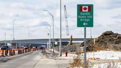 Bloomberg via Getty Images A sign for the Gordie Howe International Bridge, with a Canadian flag and an arrow pointing left, sits on the side of a highway.  