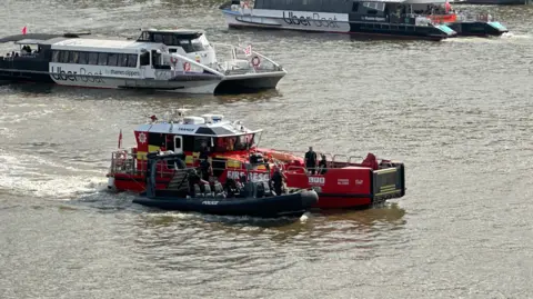 PA Media A fire service boat towing a police boat down the Thames.