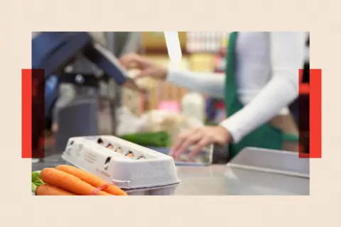 Getty Images A casher at a supermarket processes a carton of eggs and a bunch of carrots