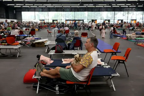AFP via Getty Images A man sits with his dog in an evacuation shelter in a gymnasium.