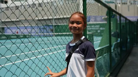 BBC/Virma Simonette Rivera Maristella Torrecampo, a Filipina tennis player and fan of Alex Eala, standing on the side of a tennis court in Manila