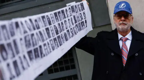 Getty Images Paul Hudson, whose daughter Melina was one of the victims in the Pan Am Flight 103 Lockerbie bombing, holds up a banner of pictures of additional victims outside the federal court before the trial for a Libyan man accused of making the bomb