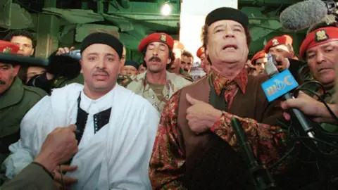 Getty Images Lockerbie bombing defendant Al-Amin Khalifa Fhimah (L) speaks to the media with Libyan leader Muammar al Gadhafi after arriving a day after being acquitted in the Lockerbie bombing trial February 1, 2001 in Libya, Tripoli.