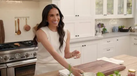 Netflix The Duchess of Sussex in a kitchen smiling and wearing a white outfit