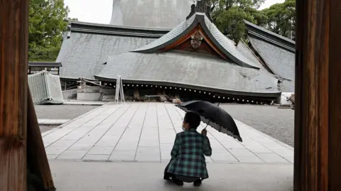 Reuters A woman with an umbrella squats in front of a collapsed shrine