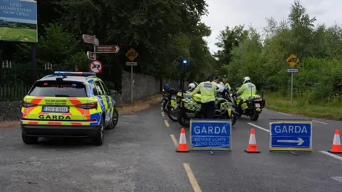 PA Media Police officers at the scene of the fatal crash in Dublin. Two of the officers are on  motorbikes and a Garda car is also visible as are two blue Garda signs