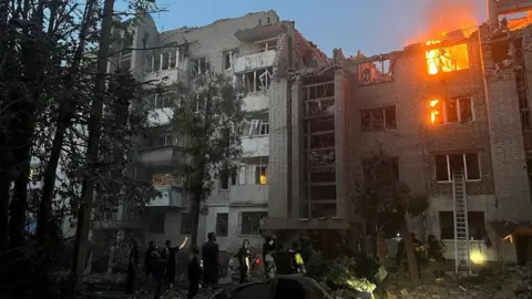 Reuters Firefighters work at a site of a building damaged by a Russian missile strike, amid Russia's attack on Lviv, Ukraine. A building is damaged and on fire, with firefighters standing in the foreground. 
