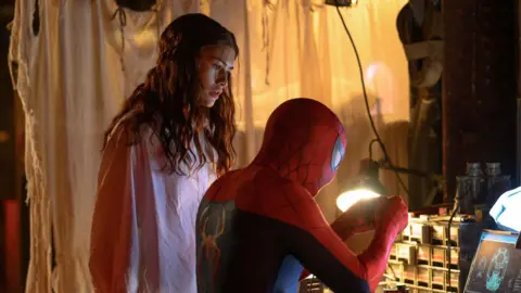 Sony Pictures/Marvel Zendaya as MJ watching Spider-Man, played by her husband Tom Holland, working with his hands while sat as a desk