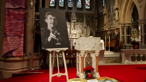 PA Media A black and white picture of Shane MacGowan holding a glass of wine at a church where his funeral took place