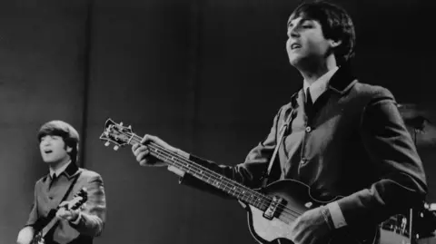 John Lennon left and Paul McCartney right singing in a black and white picture from 1964