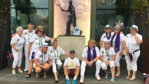 Supplied Geoff Hughes is sitting in the middle of a photo in front of a Fred Perry statue surrounded by members of the Andy Murray fan group The Murraynators