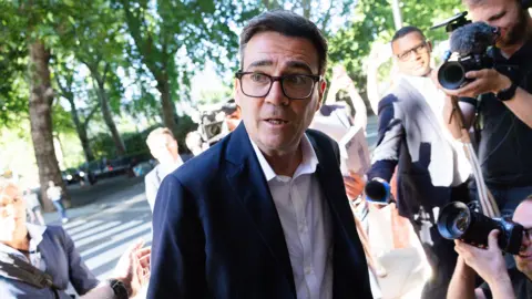 AFP via Getty Images Andy Burnham looks to the left of frame while wearing a suit and shirt and surrounded by cameras and reporters, as he arrives at Millbank on 2 July