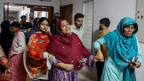 AFP via Getty Images A tearful woman walks along a hospital corridor, held by two other women on both sides