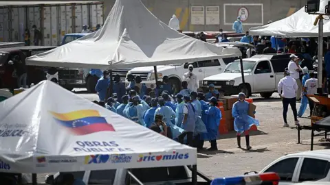 AFP via Getty Images A group of staff officers in blue protective wear stand beneath a white tent