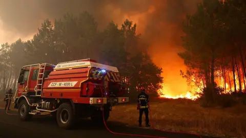 AFP via Getty Images Firefighters try to extinguishing fires burning trees using a wildland water truck. The flames can be seen in the forested area