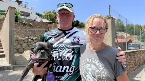 BBC A man, holding a dig and wearing a Thai sports shirt with Chang beer as a sponsor, puts his arm round a woman wearing an olive green T-Shirt