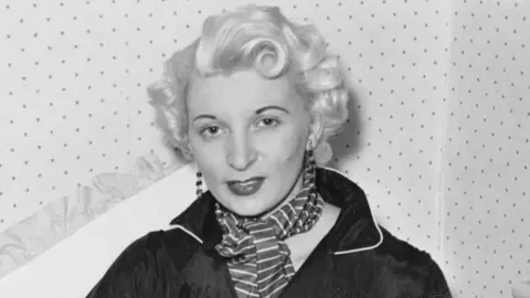 Bettmann Archive/Getty Images Ruth Ellis poses for a photograph - the black and white picture shows her with white-blonde hair, wearing long earrings, a striped scarf and a black shirt.