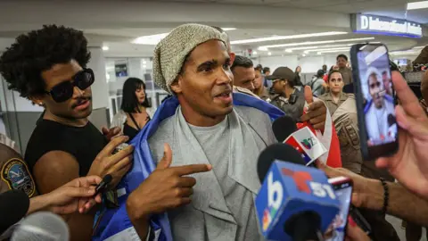 AFP via Getty Images Luis Manuel Otero Alcántara speaks to journalists at Miami airport. 