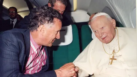 BBC David Willey, wearing a suit and a pink shirt, talks with Pope John Paul II during a plane trip back to Rome from Bulgaria 26 May 2002