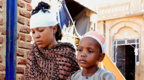 Reuters A young woman and a boy, with bandages over their heads, sit in el-Obeid city on 12 January 2026. Both sustained injuries during a drone strike.  