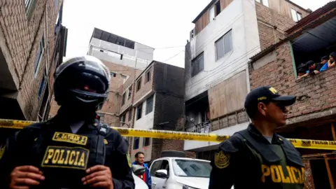 ANDINA/ Luis Iparraguirre Two police officers guard a cordoned off area, which has several apartment blocks that are about four storeys high. One of them is blackened by fire.