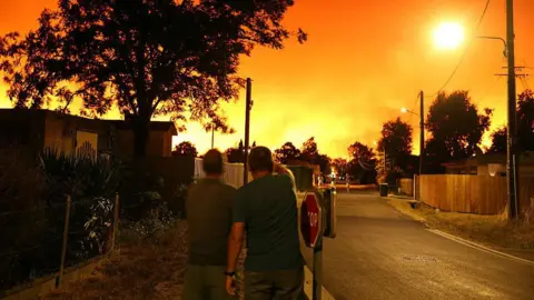 AFP via Getty Images Residents look at the sky illuminated by wildfires in Le Porge, south-western France early on July 23, 2026.