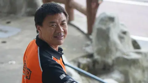 Xinhua Wang Jibing in an orange polo shirt smiling at the camera