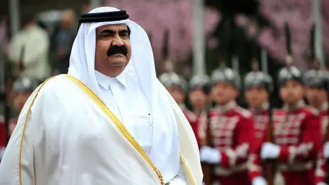 Getty Images Hamad is seen wearing a white robe as uniformed military guards stand to attention behind him.
