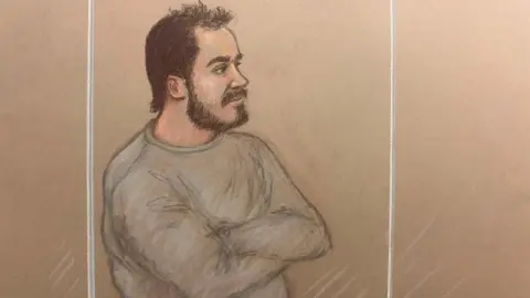 Julia Quenzler/BBC A man with short brown hair and a beard is pictured looking on in a dock while wearing a grey sweatshirt in a court sketch 