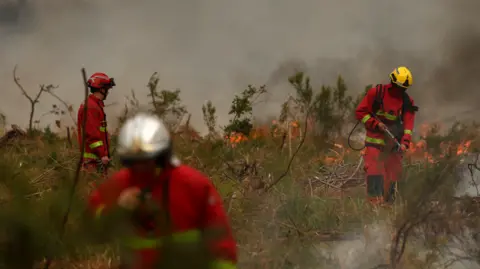 Getty Images Firefighters of Paris Fire Brigade survey the scene amid the smoke and fire in Marcheprime west of Bordeaux on July 26, 2026 as a wildfire has been ravaging the forest north of the Arcachon Basin (Gironde) since July 22. The fire that has engulfed the area around the Arcachon Basin and is now threatening the outskirts of the Bordeaux metropolitan area has destroyed 42,000 hectares of "burned area," the Gironde prefecture announced; the prefecture has evacuated a total of 220,000 people since July 22. 