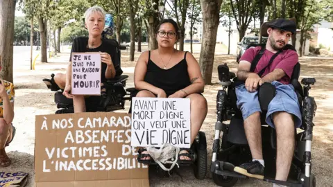 EPA Protesters in wheelchairs  hold up signs reading "I am not a reason to die " and  "Before a dignified death, I want to see a dignified life"
