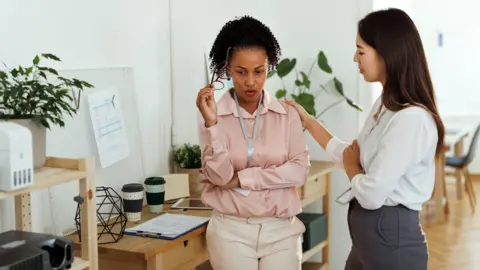Getty Images Stock photo shows two workers in an office, one looking visibly unwell, and the other consoling them. 
