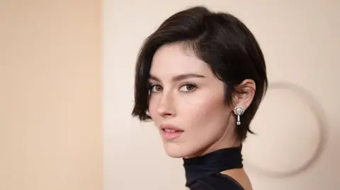 Getty Images Gracie Abrams poses on the red carpet of the 2026 Oscars, in a black dress with a choker, and sparkling diamond earrings.